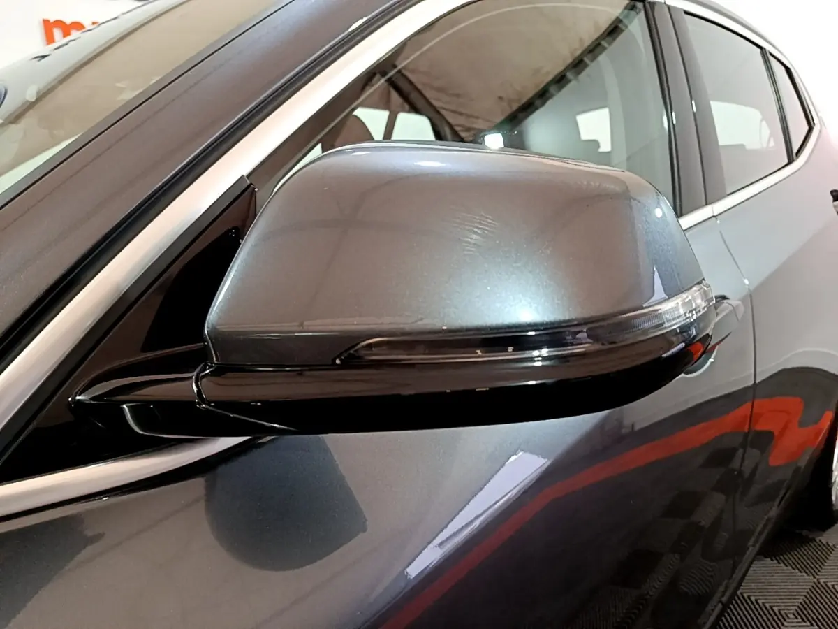 Gros plan sur le rétroviseur droit gris foncé d'une BMW X2 sDrive18i Lounge DKG7, avec la porte arrière visible en arrière-plan.