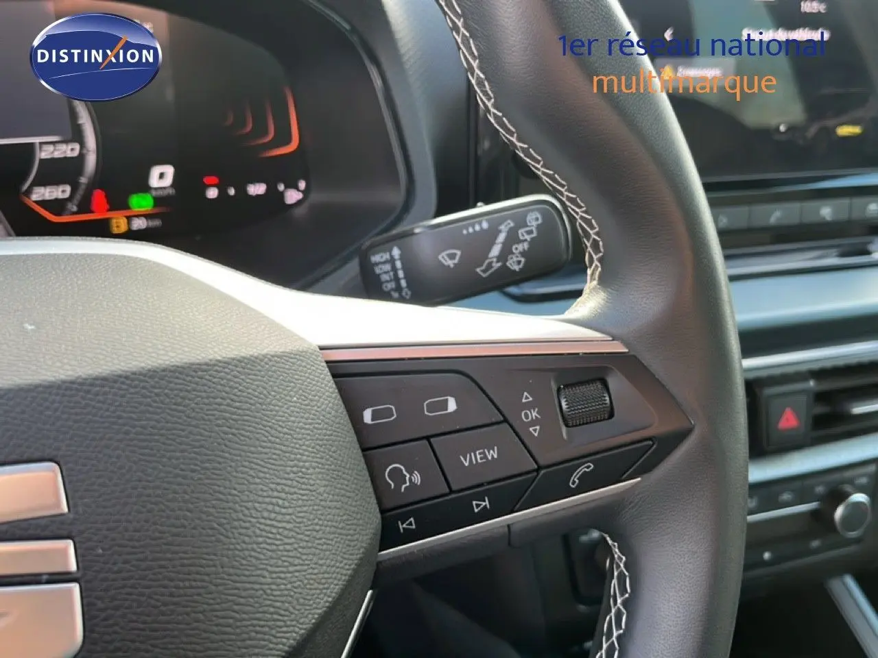 Gros plan sur le volant noir avec surpiqûres blanches du SEAT Arona 2025, montrant les commandes multifonctions côté droit.