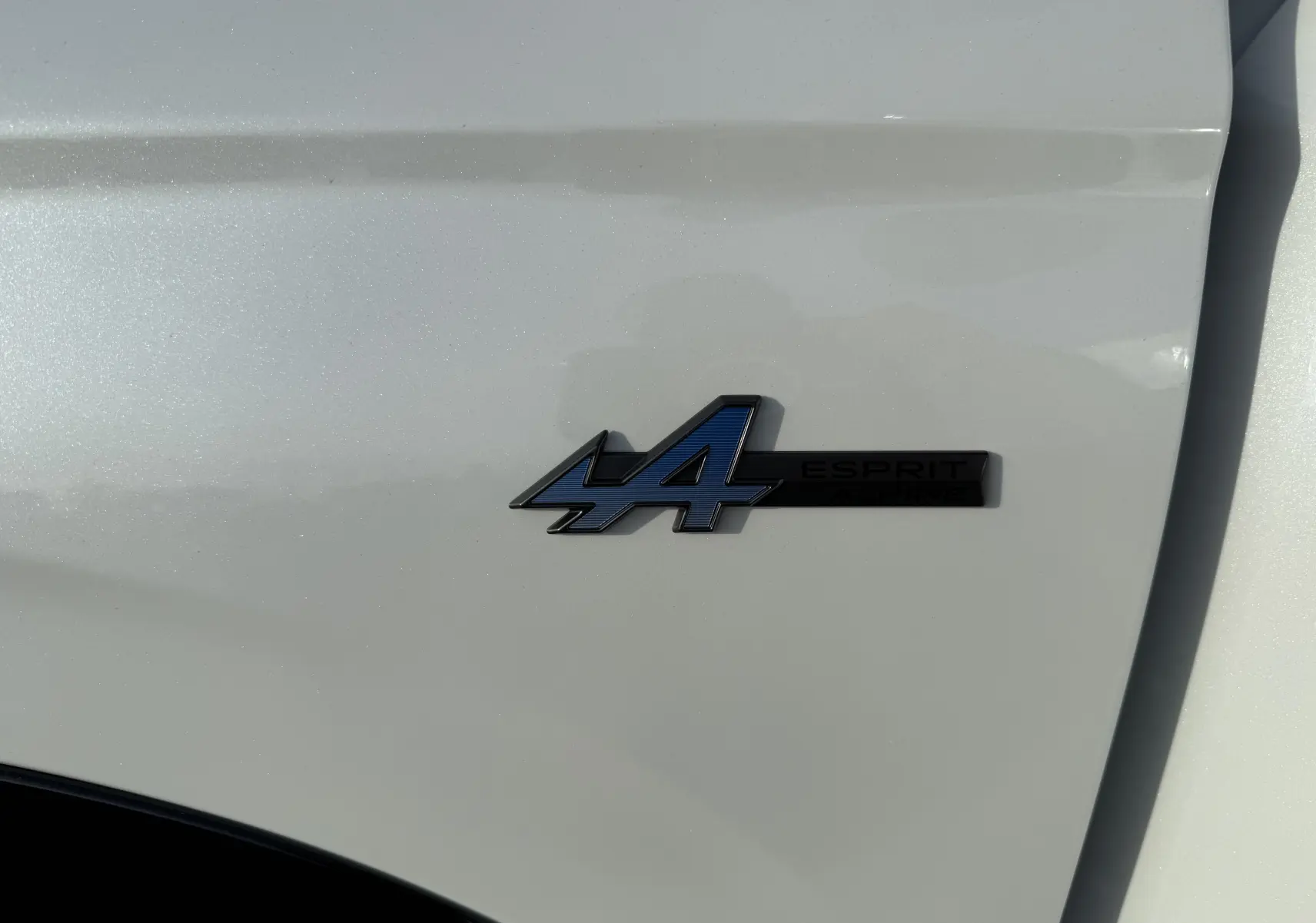 Gros plan sur l'écusson Esprit Alpine bleu et noir sur la porte blanche nacrée du Renault Austral 2025.