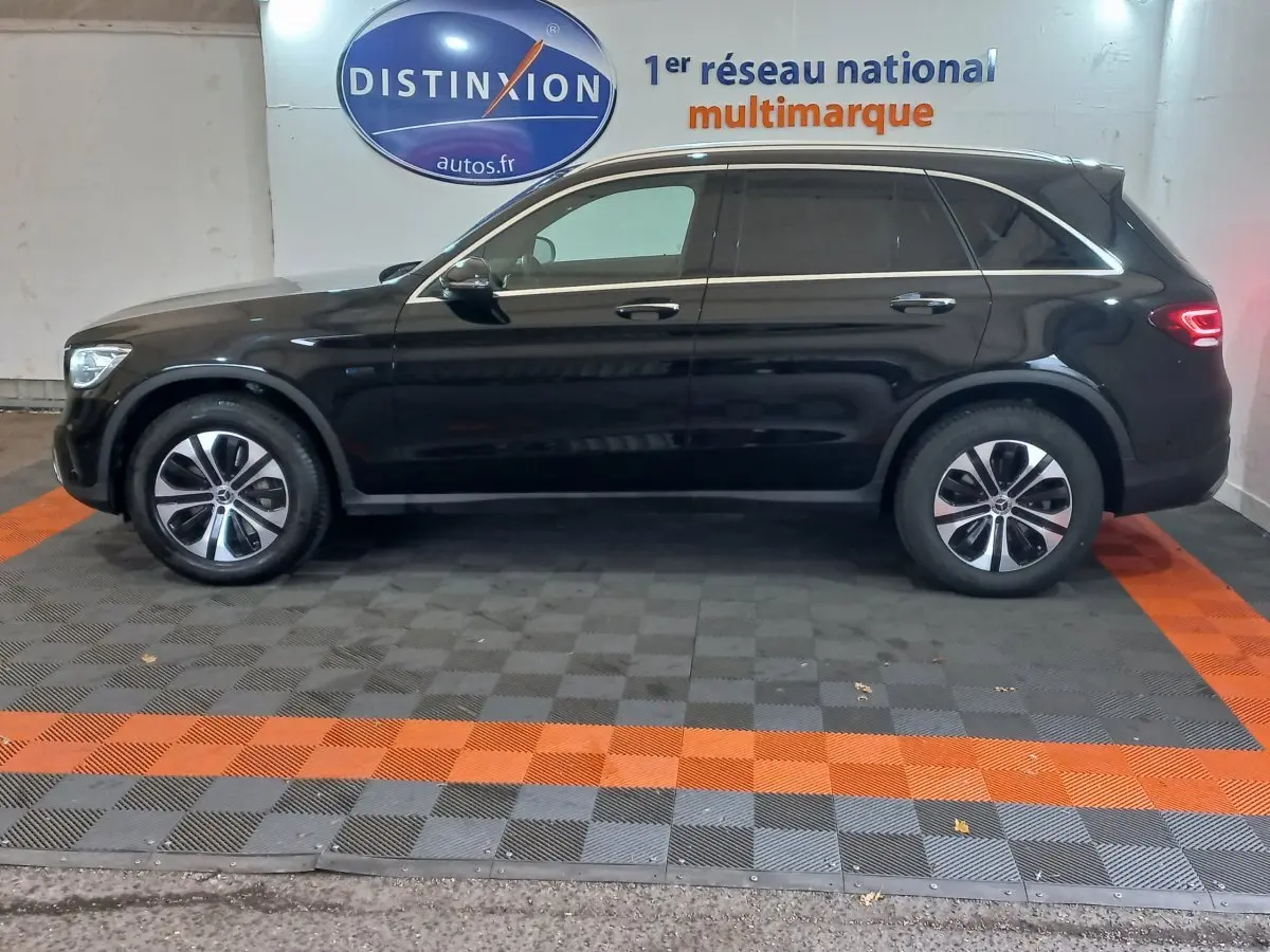 Profil côté gauche d'un Mercedes GLC 300 E Business Line hybride rechargeable noir, stationné en intérieur sur sol damier.