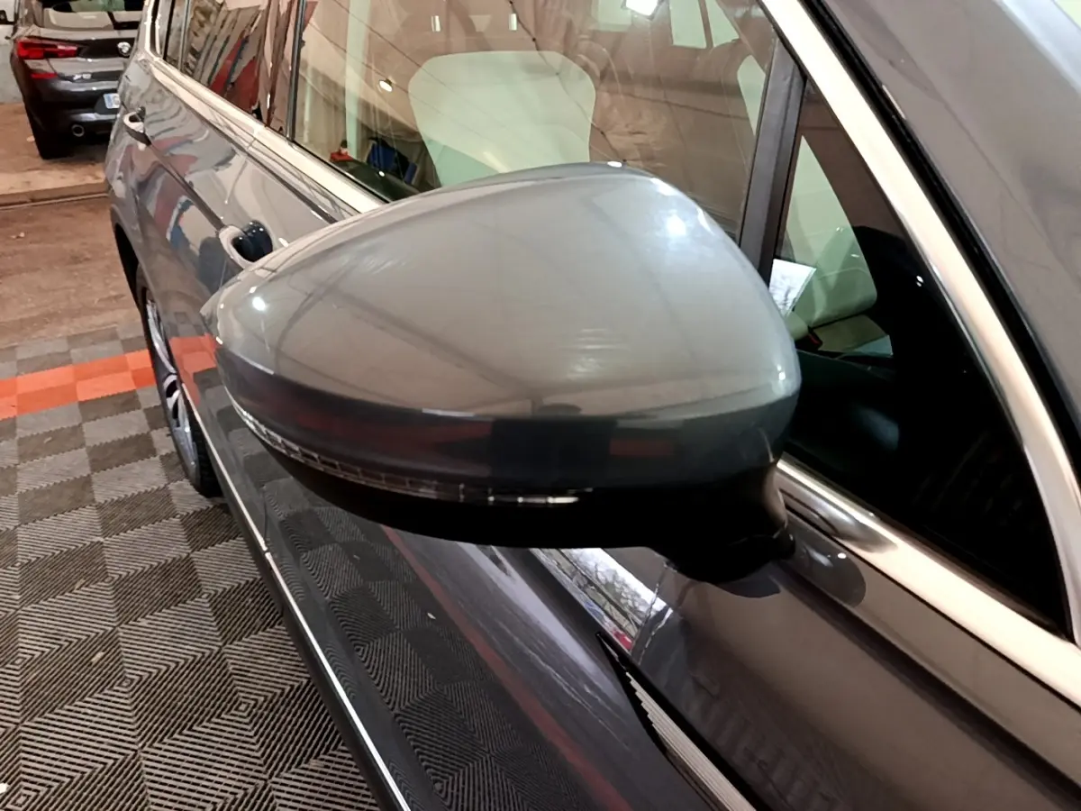 Gros plan sur le rétroviseur côté gauche gris clair du Volkswagen Tiguan 2022 dans un garage intérieur.