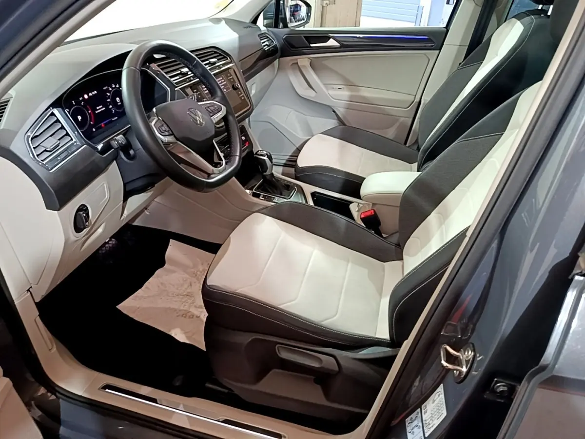 Vue intérieure côté conducteur du Volkswagen Tiguan gris clair 2022, avec sièges bicolores et tableau de bord digital.
