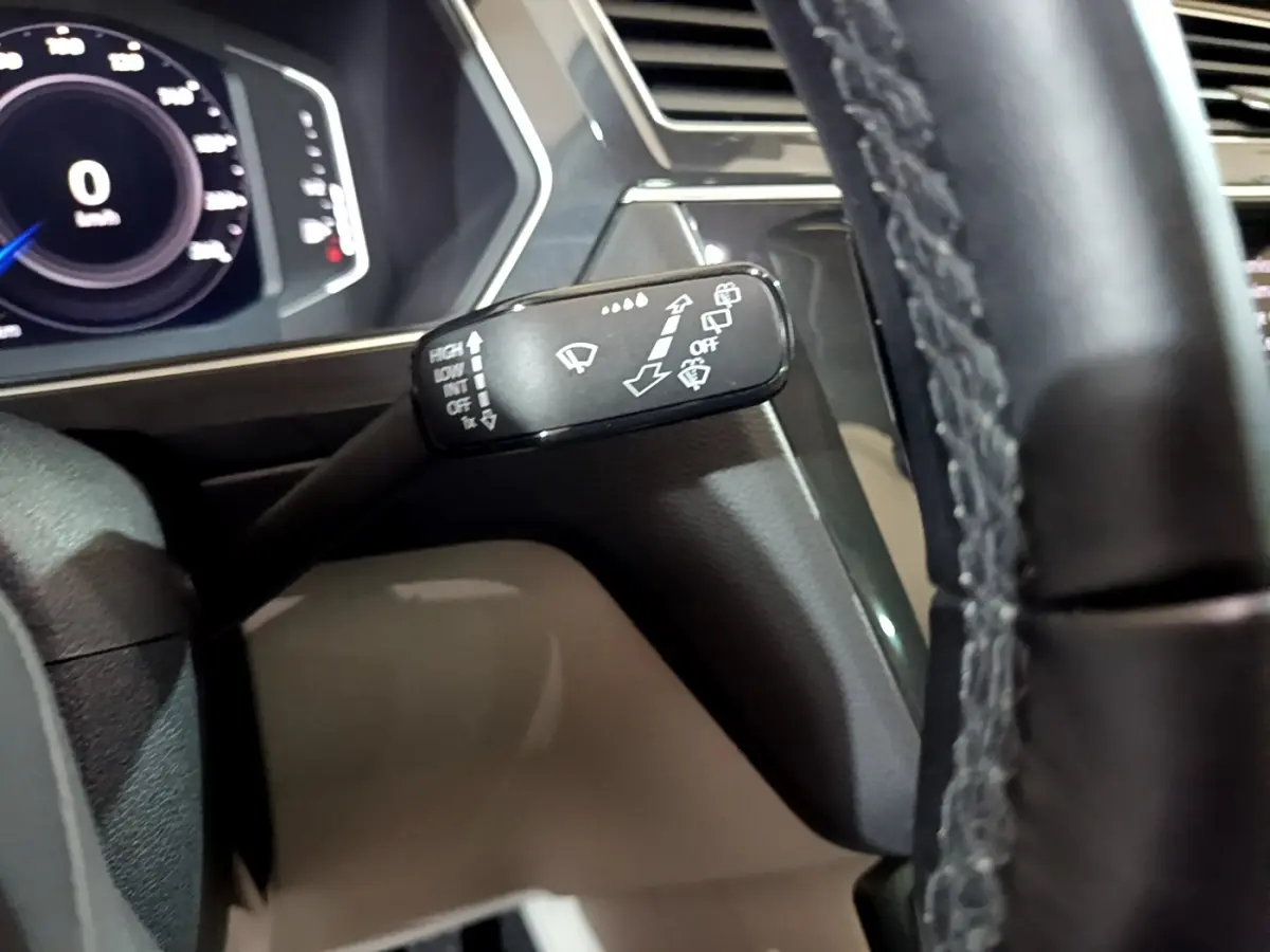 Gros plan sur la manette d’essuie-glace à gauche du volant cuir dans l’habitacle du Volkswagen Tiguan gris clair.