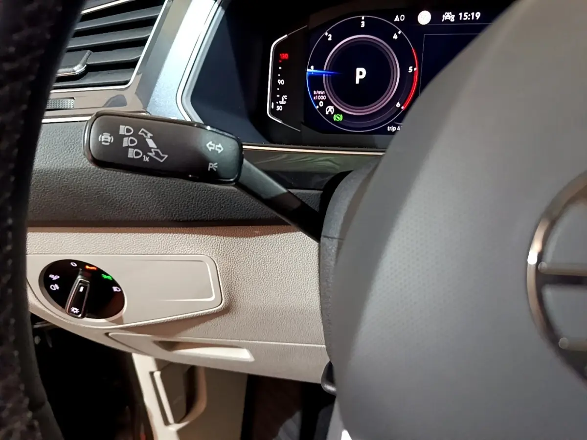 Détail intérieur du volant et levier de clignotant du Volkswagen Tiguan gris clair, avec tableau de bord numérique visible.