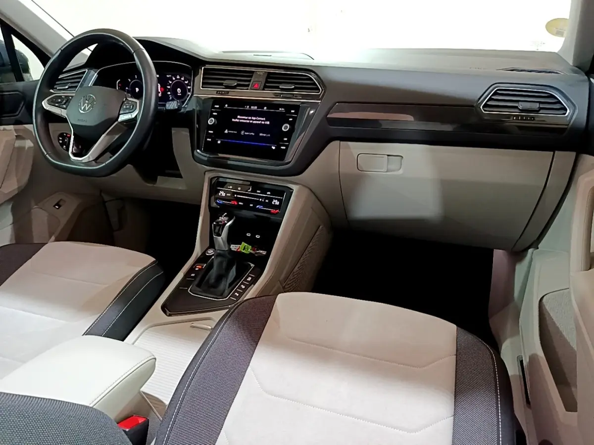 Vue intérieure avant du Volkswagen Tiguan 2.0 TDI gris clair, avec tableau de bord moderne et écran tactile central.