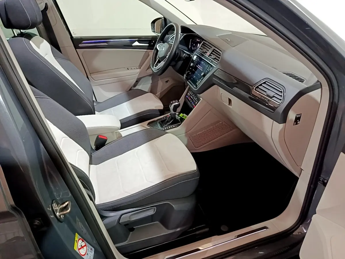 Vue intérieure côté conducteur du Volkswagen Tiguan gris clair 2022, sièges bicolores et tableau de bord moderne avec écran tactile.