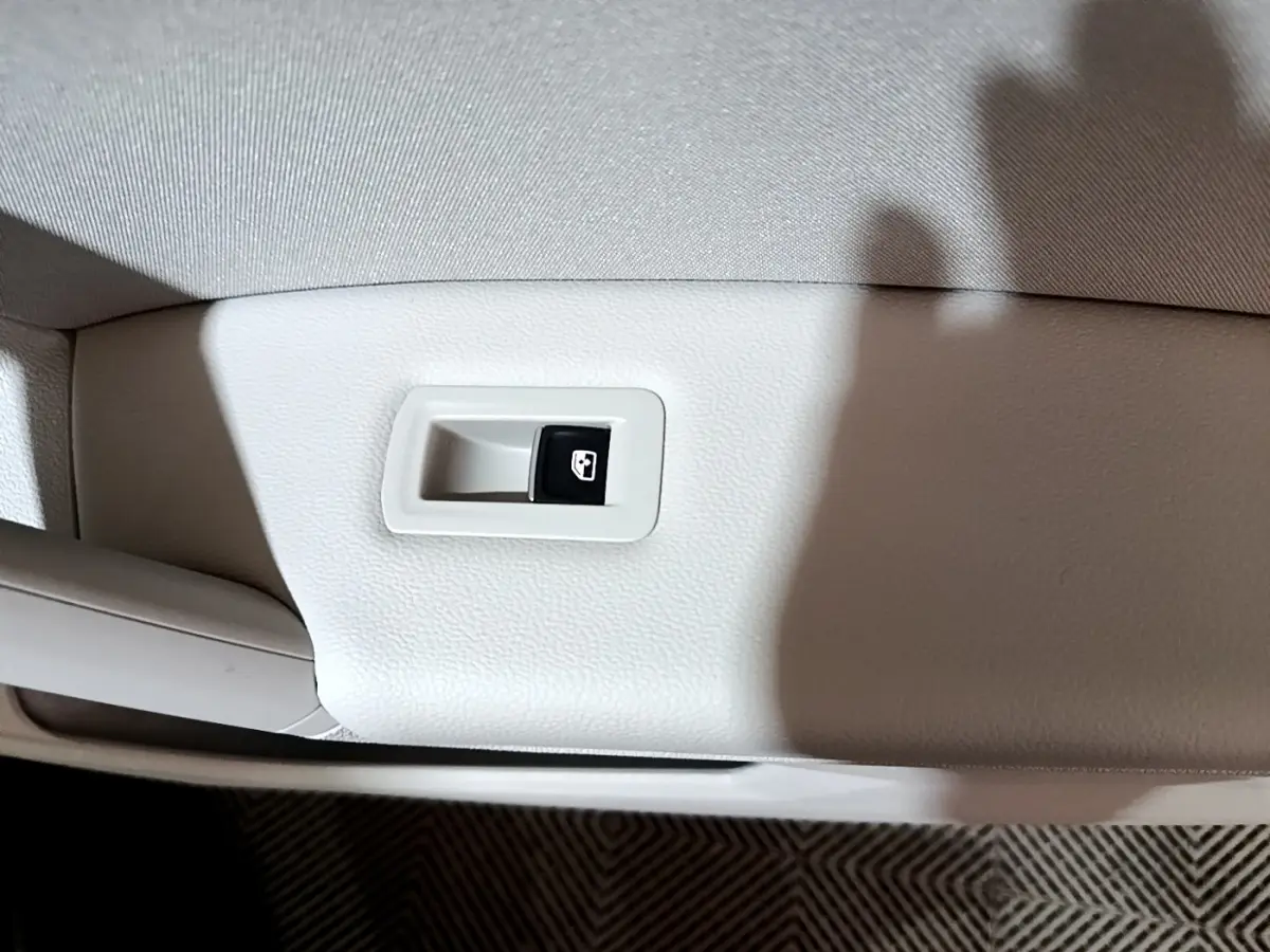 Gros plan sur le bouton de commande de vitre électrique sur la porte intérieure beige d'un Volkswagen Tiguan gris clair.