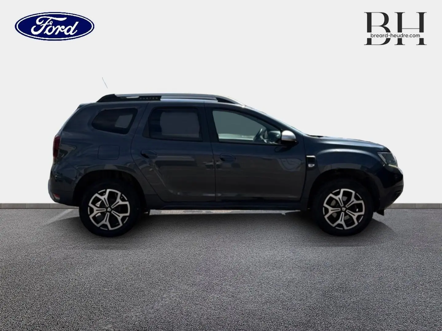 Profil côté gauche du Dacia Duster 2020 gris Comète métallisé avec jantes alu et barres de toit visibles.