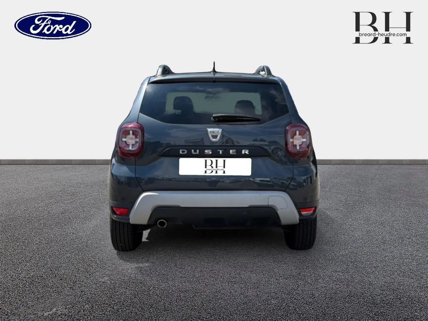 Vue arrière du Dacia Duster gris Comète métallisé avec barres de toit et sortie d'échappement chromée visible.