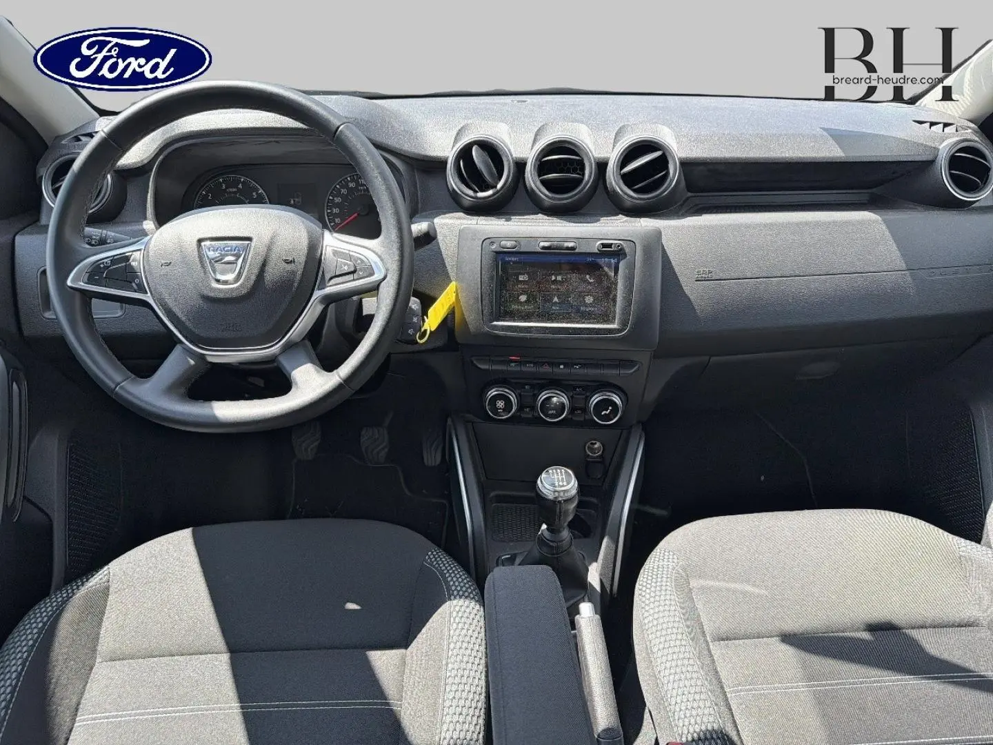 Intérieur avant du Dacia Duster 2020 en tissu gris, vue centrée sur le tableau de bord et la boîte manuelle.