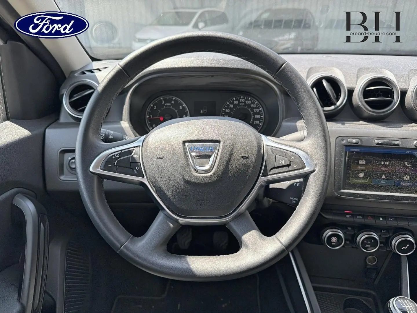 Vue intérieure centrée sur le volant Dacia du Duster 2020, avec commandes multifonctions et tableau de bord visible.