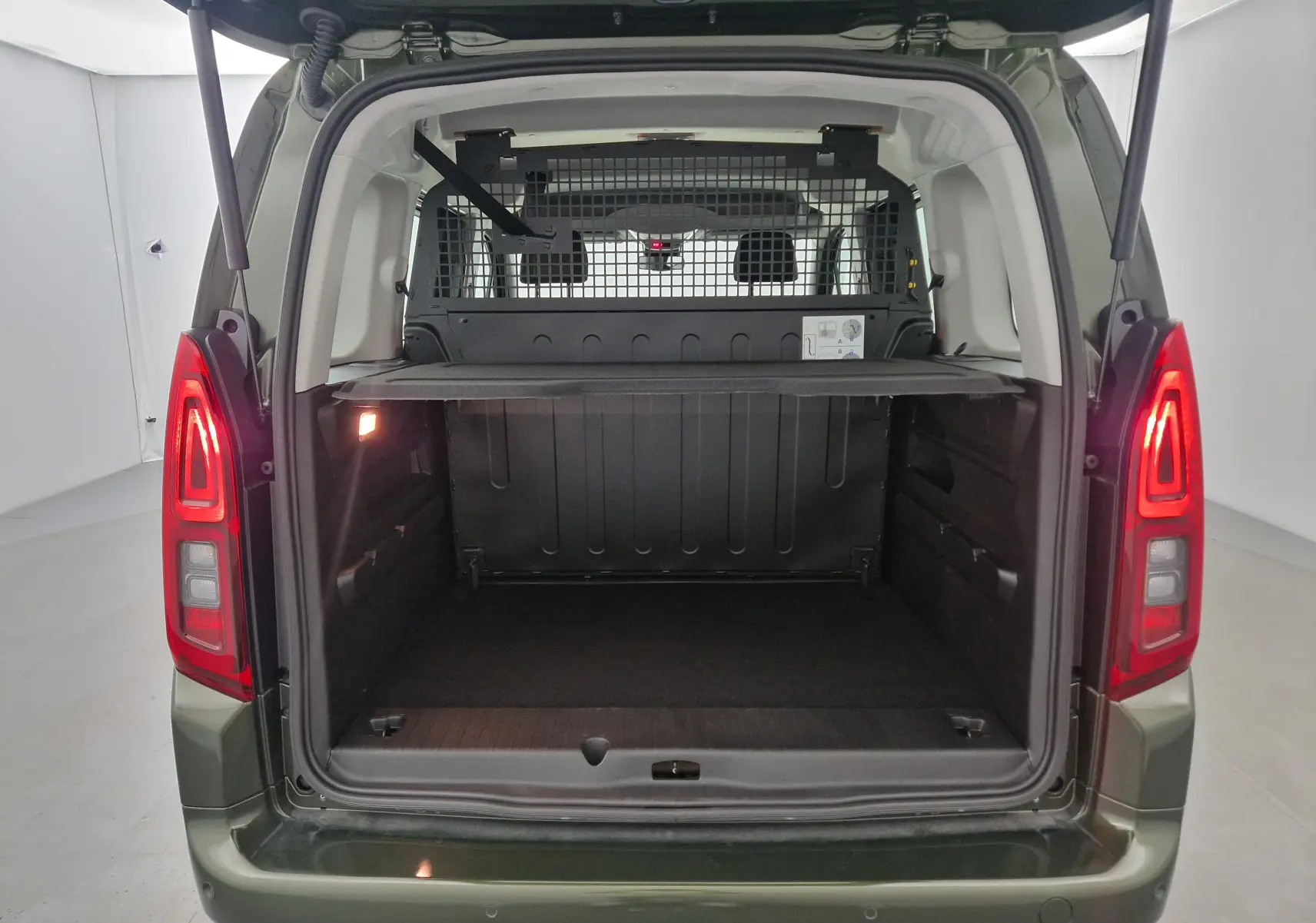 Vue arrière ouverte de l'Opel Combo Life vert Sirkka montrant le coffre spacieux avec grille de séparation et éclairage intérieur.