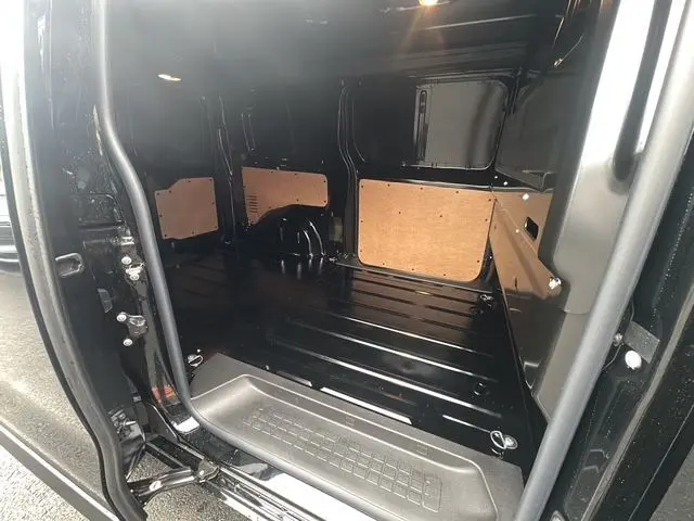 Intérieur du coffre noir du Citroën Jumpy 2025, vue depuis la porte latérale ouverte, avec panneaux de protection en bois.