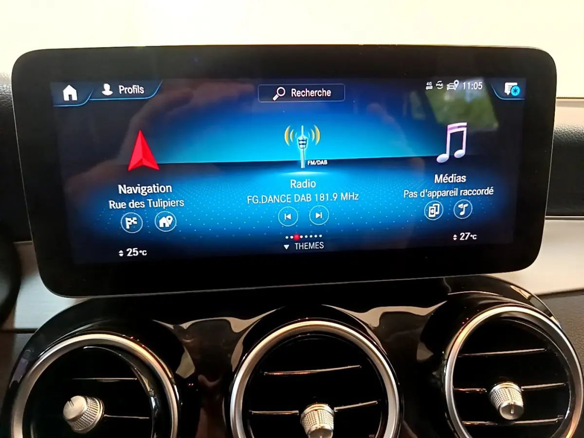 Écran tactile central affichant navigation, radio et médias, avec trois aérateurs ronds chromés en dessous dans un Mercedes GLC 2021.