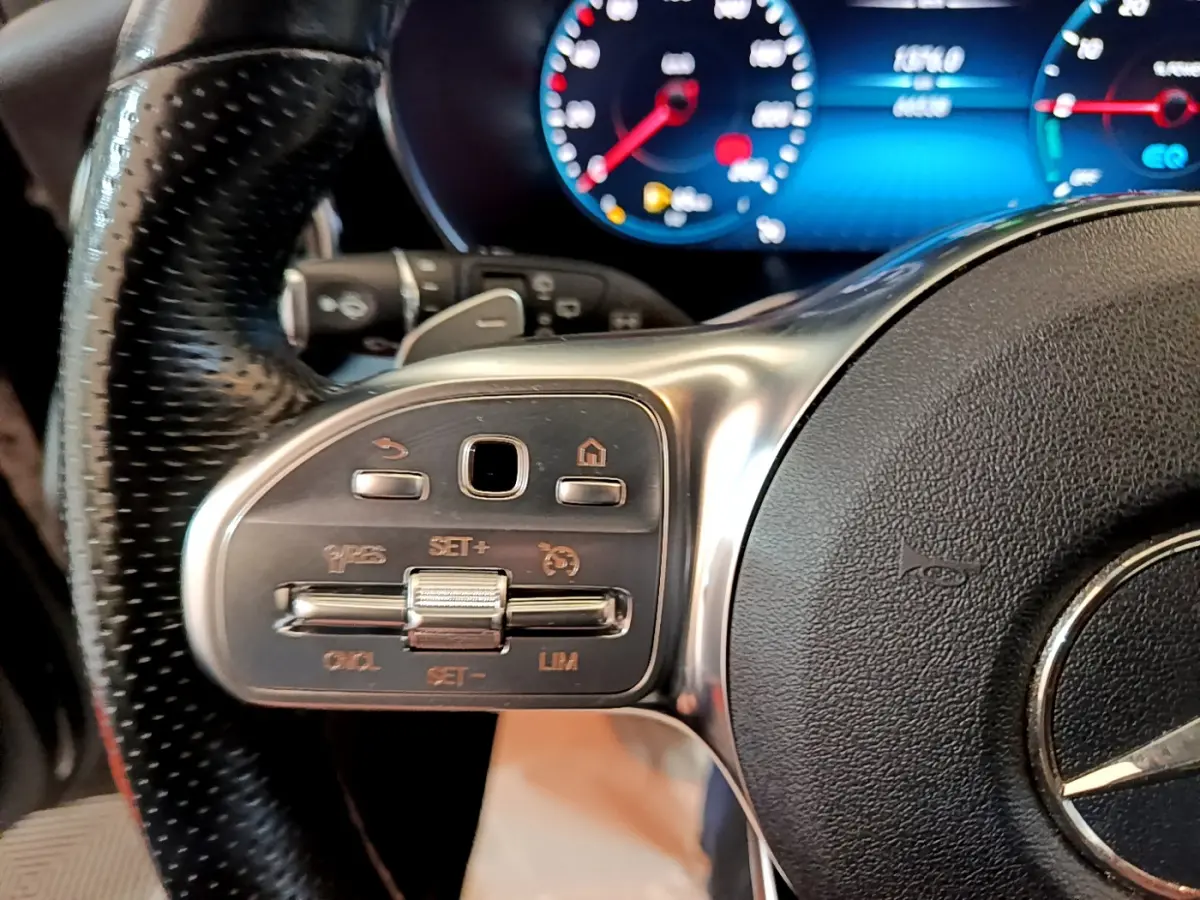 Gros plan sur le volant cuir et alu du Mercedes GLC 300 E AMG Line 2021 avec commandes intégrées et tableau de bord numérique bleu.