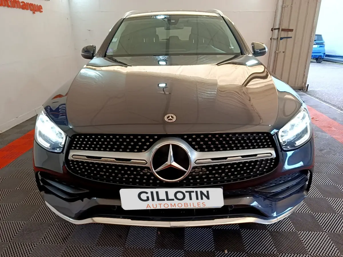 Vue avant d'un Mercedes GLC 300 E AMG Line gris foncé avec phares LED allumés en intérieur showroom.