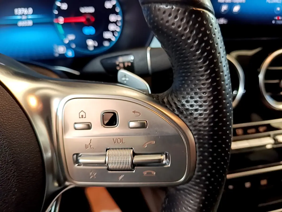 Gros plan sur les commandes du volant cuir perforé du Mercedes GLC 300 E AMG Line 2021, tableau de bord numérique en arrière-plan.