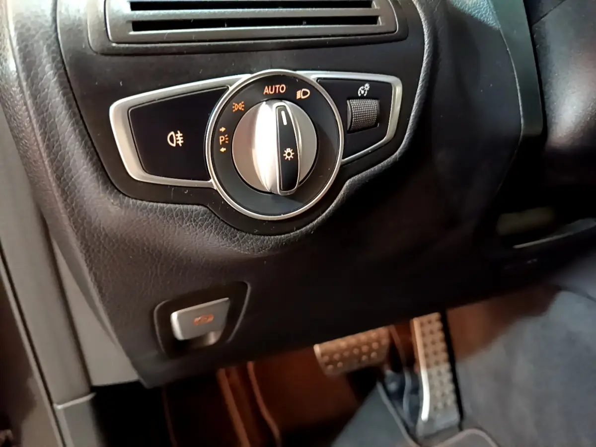 Gros plan sur la commande des phares et le bouton de frein de stationnement dans l'habitacle noir du Mercedes GLC 300 E AMG Line.