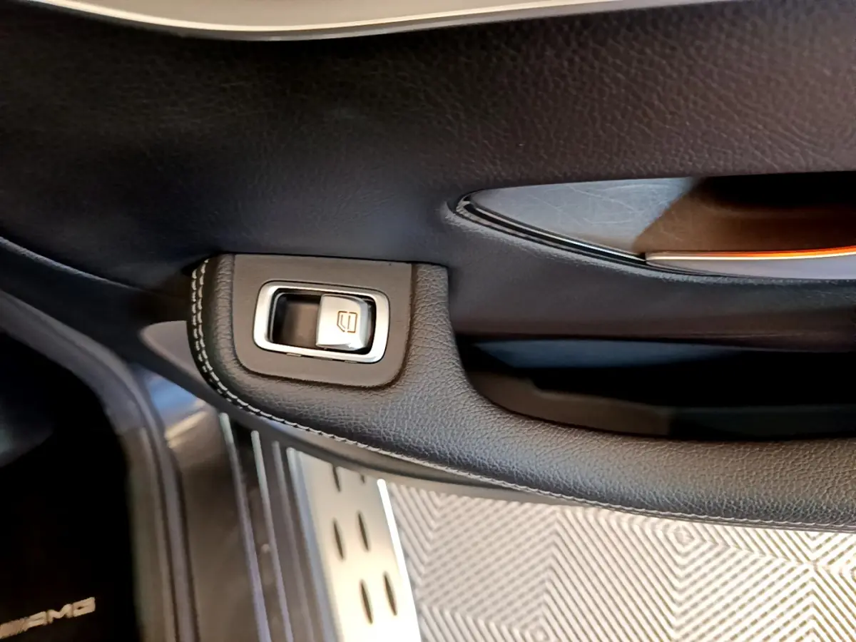 Gros plan sur la commande de lève-vitre en cuir noir avec surpiqûres dans une Mercedes GLC 300 E AMG Line gris foncé.