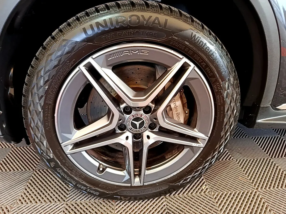 Gros plan sur la jante AMG gris foncé avec logo Mercedes et pneu hiver Uniroyal sur un Mercedes GLC hybride rechargeable.