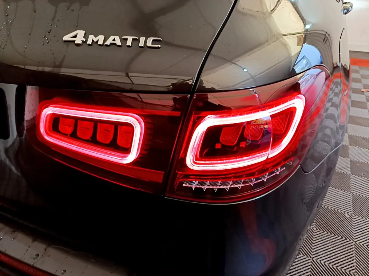 Gros plan sur le feu arrière droit rouge allumé et le logo 4MATIC sur la carrosserie gris foncé d'un Mercedes GLC hybride.