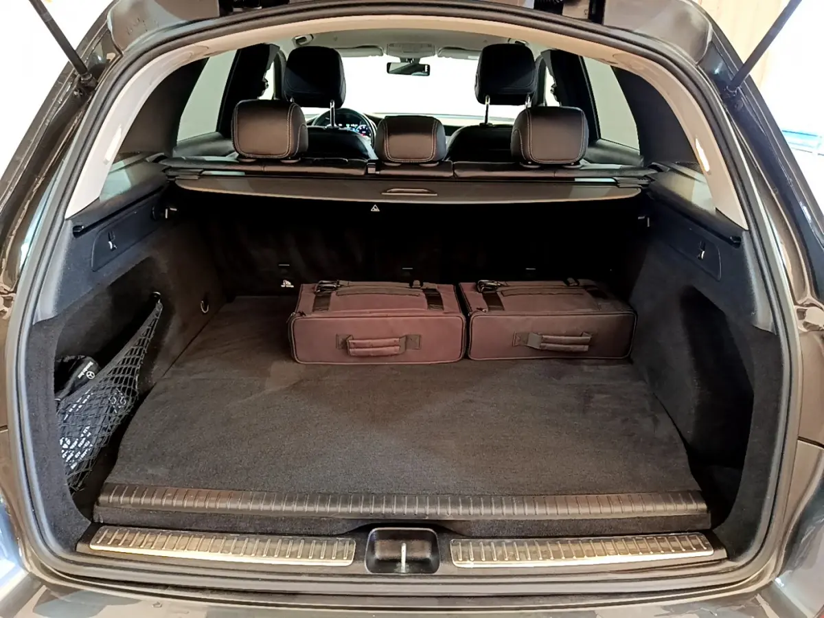 Coffre ouvert du Mercedes GLC 300 E AMG Line gris foncé, avec deux valises noires et banquette arrière visible.