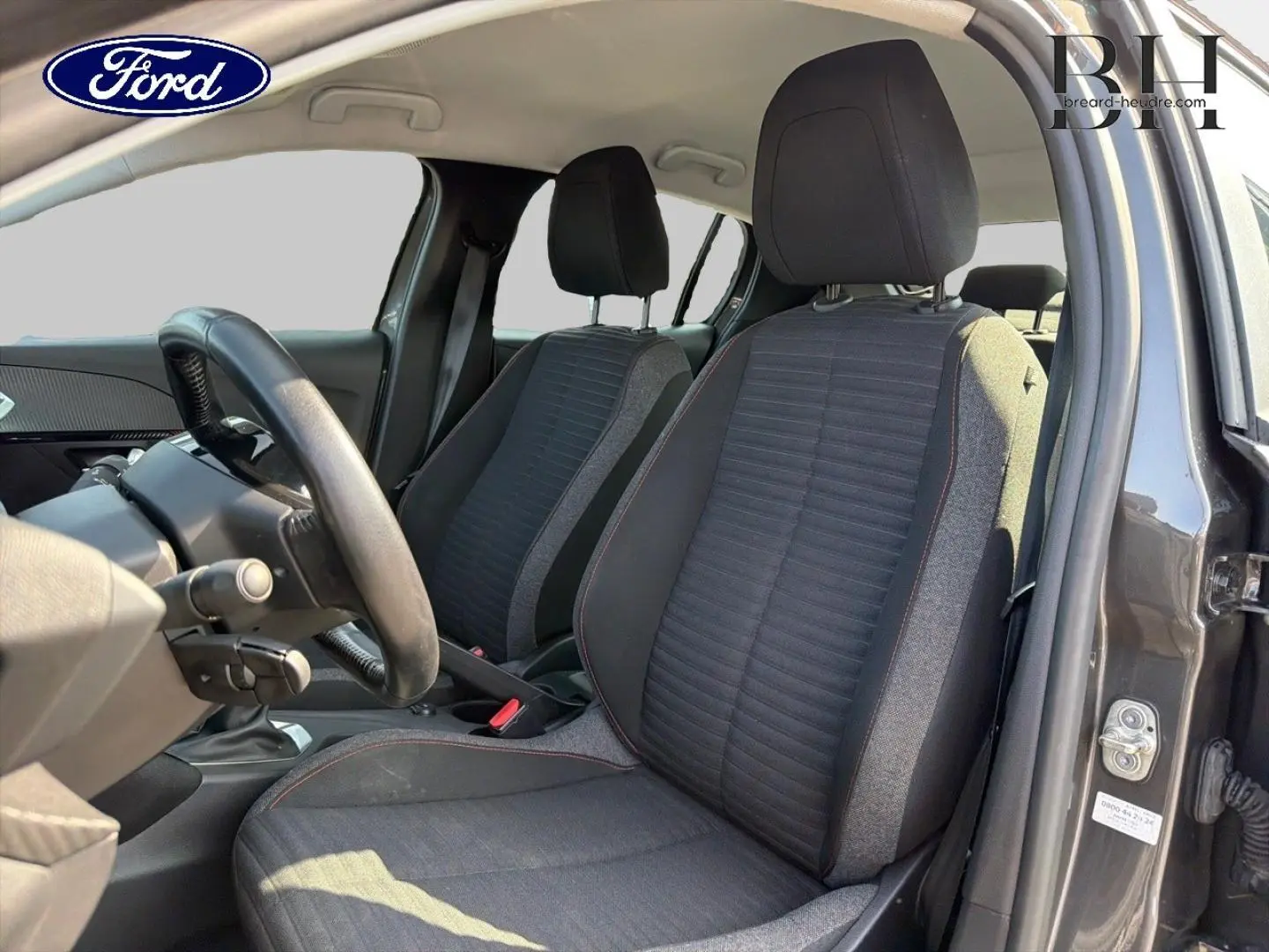 Vue intérieure côté conducteur de la Peugeot 208 1.5 BlueHDi gris Platinium, montrant les sièges avant et le volant.