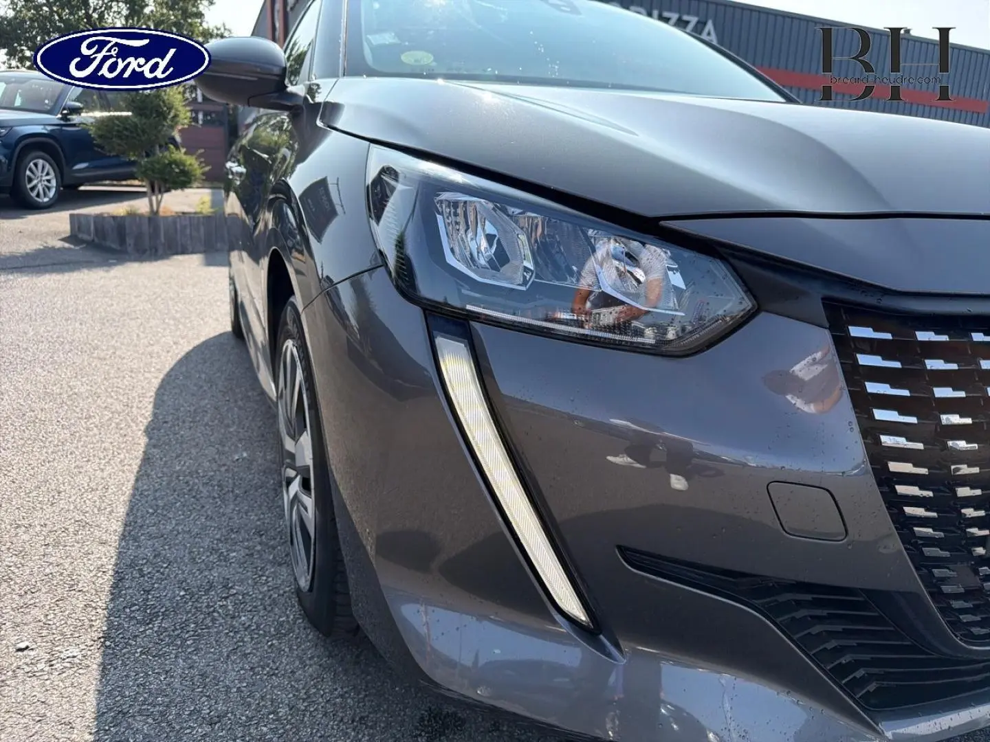 Vue 3/4 avant gauche d'une Peugeot 208 gris Platinium avec phares et calandre distinctifs visibles.
