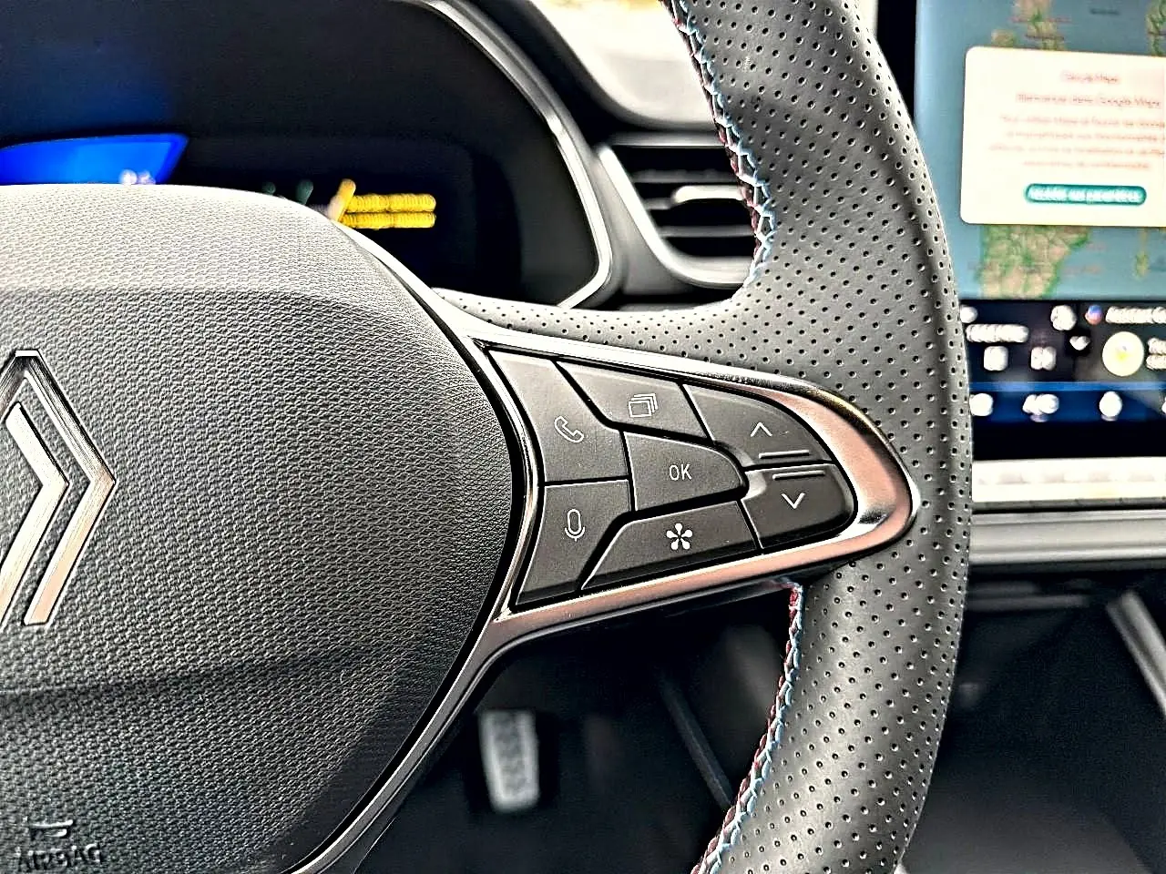 Gros plan sur le volant perforé avec commandes multifonctions du Renault Symbioz 2026, intérieur noir et écran tactile visible.