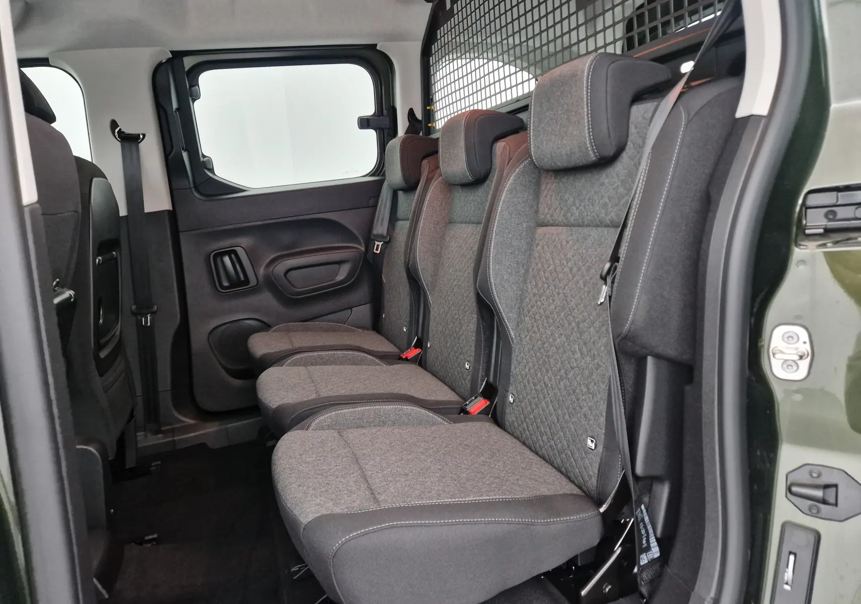 Vue latérale des trois sièges individuels arrière gris dans l'habitacle d'un Opel Combo Life vert Sirkka avec grille de séparation.