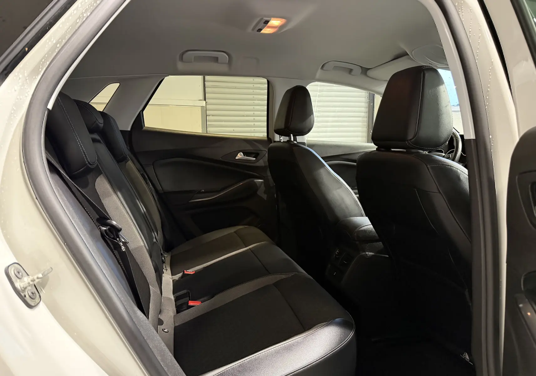 Vue intérieure côté gauche sur les sièges arrière noirs d’un Opel Grandland X blanc, avec porte arrière ouverte.