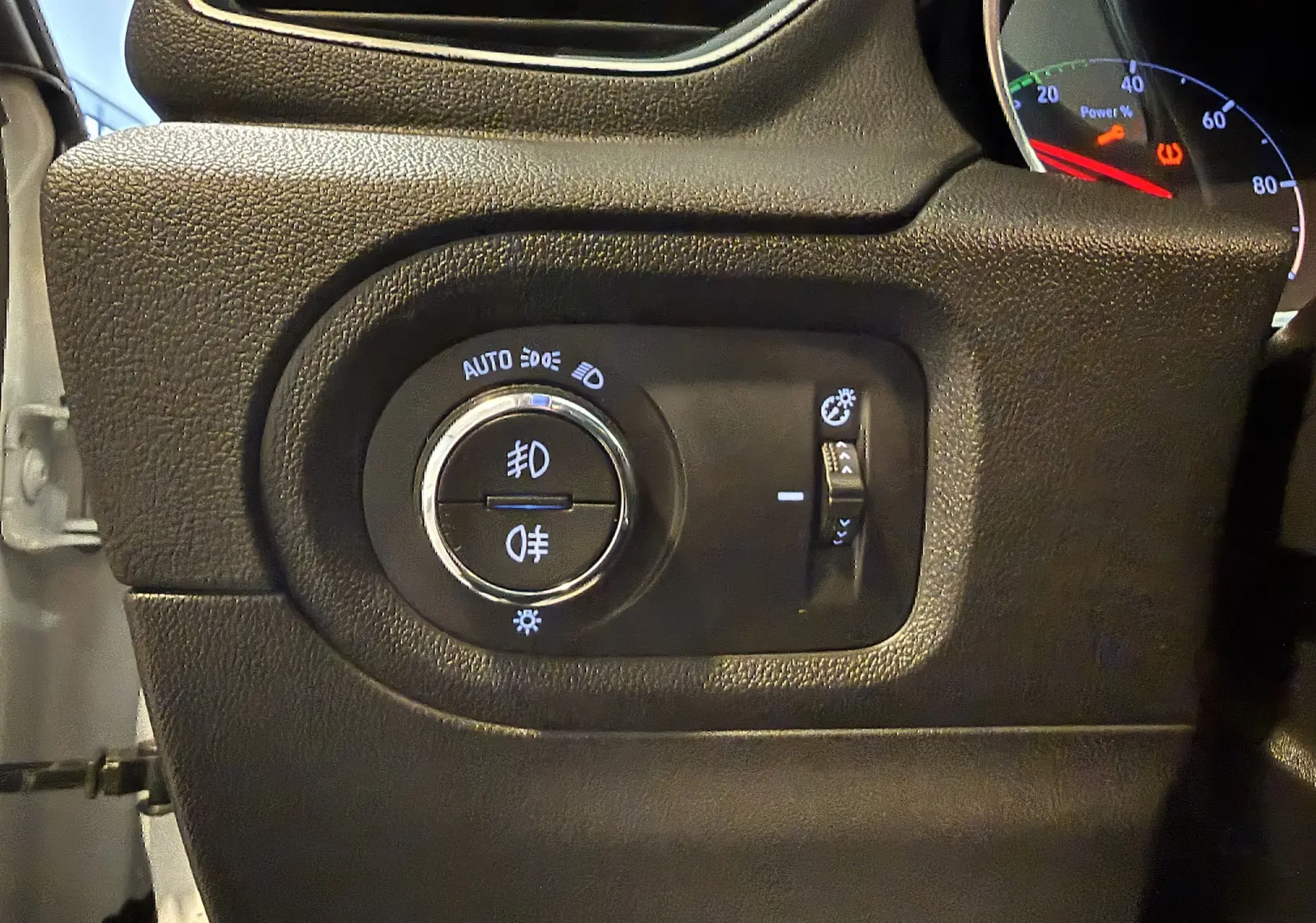Gros plan sur le panneau de commande des phares noir à gauche du tableau de bord d’un Opel Grandland X blanc.