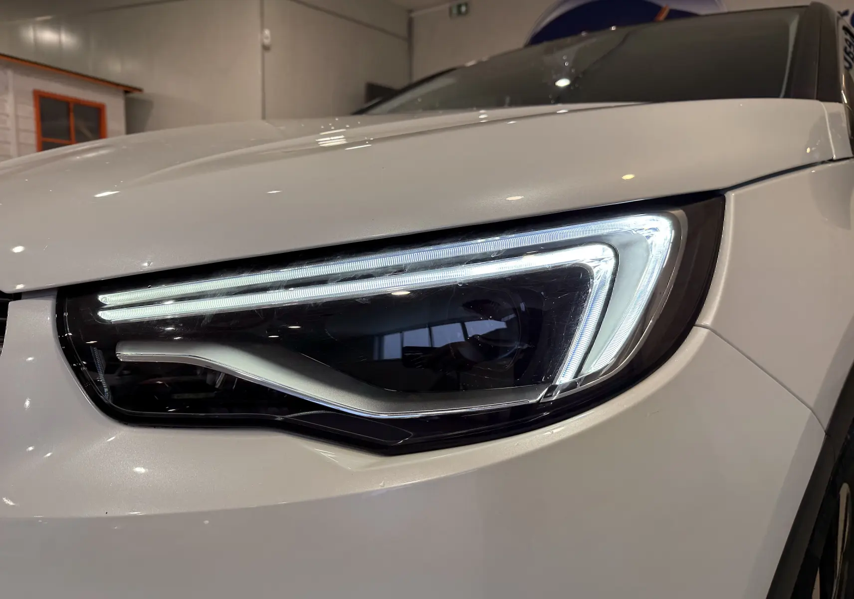 Gros plan sur le phare avant droit allumé d’un Opel Grandland X blanc, mettant en valeur son design LED moderne.