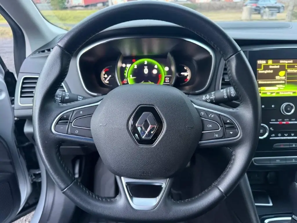 Vue centrée sur le volant noir de la Renault Mégane Business, avec tableau de bord numérique et écran tactile en arrière-plan.