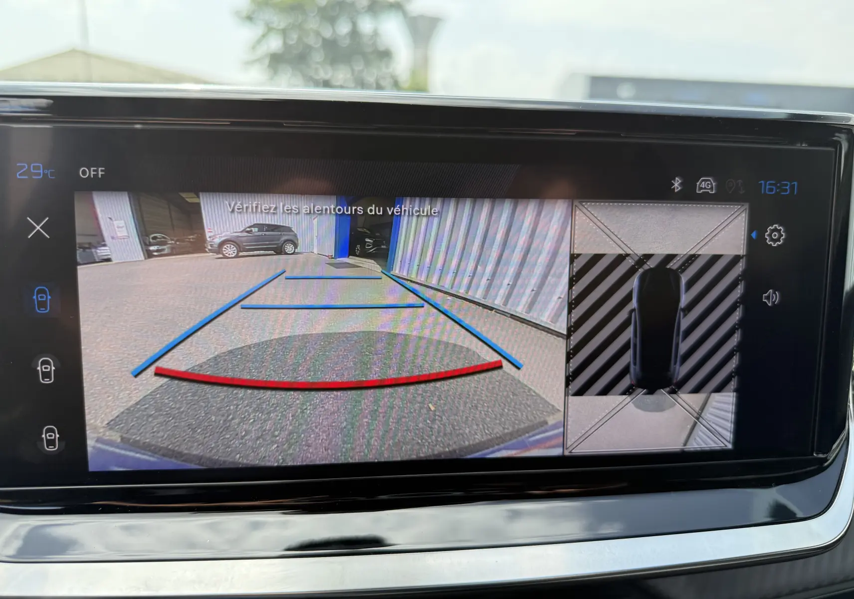 Vue écran caméra de recul et vue 360 du Peugeot 208 gris Artense stationné près d'un bâtiment industriel.