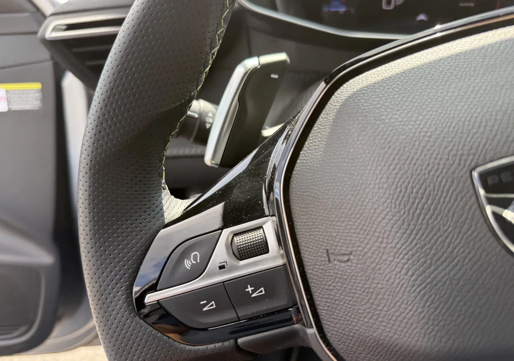 Gros plan sur le volant cuir noir perforé côté gauche du Peugeot 208 Hybrid 145 GT 2024 avec commandes intégrées.