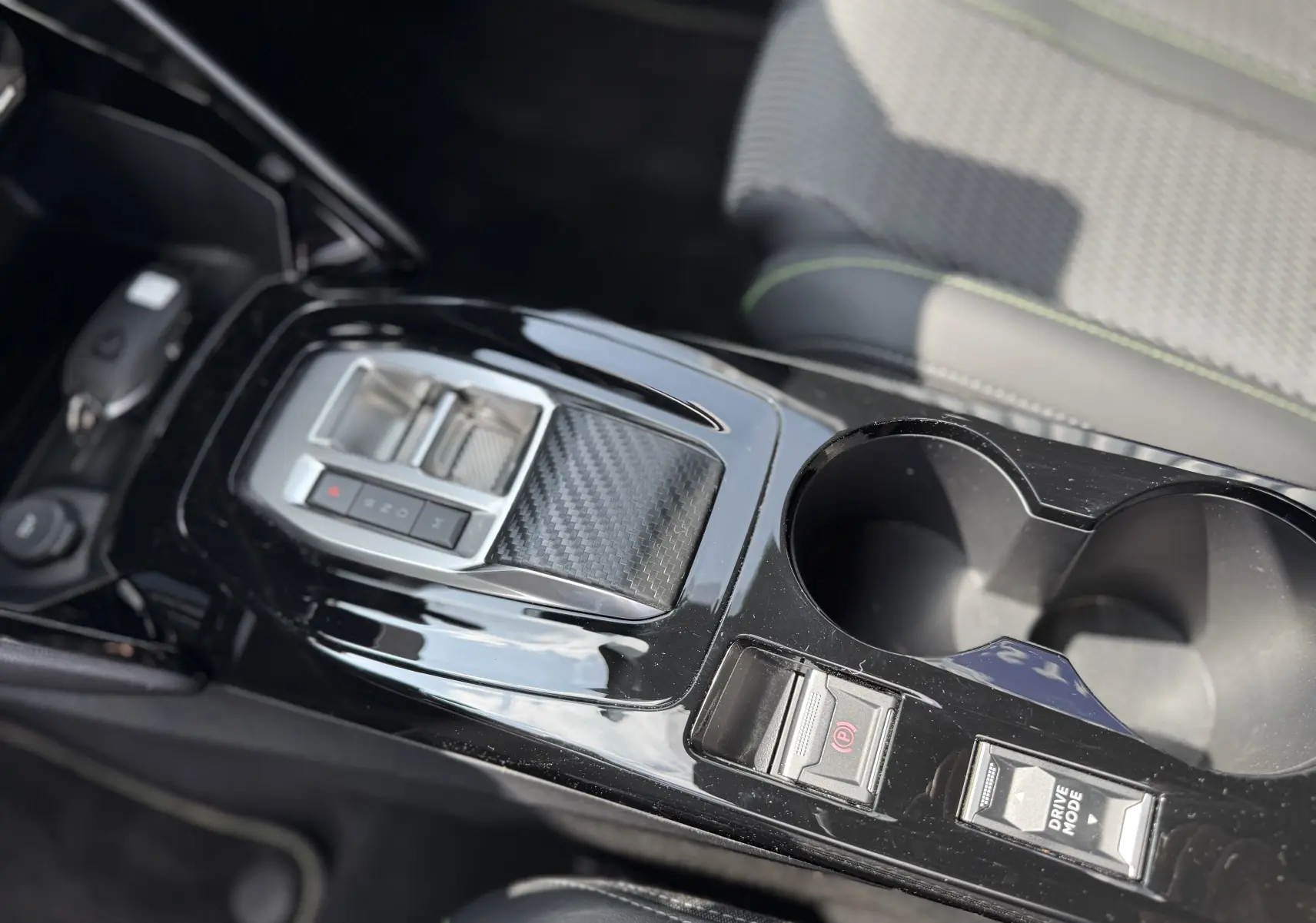 Vue rapprochée de la console centrale noire brillante de la Peugeot 208 Hybrid 145 GT avec commandes électroniques et porte-gobelets.