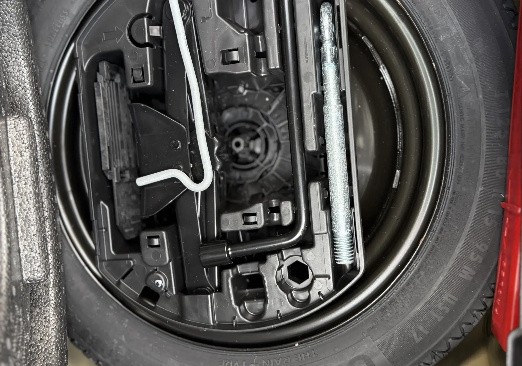 Gros plan sur la roue de secours et les outils de bord du coffre d'une Peugeot 208 Hybrid 145 GT Gris Artense 2024.