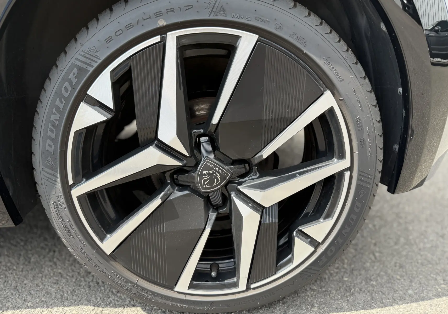 Gros plan sur la jante noire et argentée de la Peugeot 208 HYBRID 145 GT E-DCS6 gris Artense de 2024.