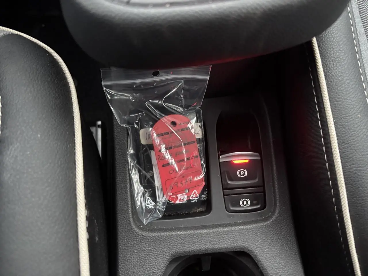 Gros plan sur la console centrale de la Renault Clio rouge flamme, avec bouton de frein à main électronique allumé.