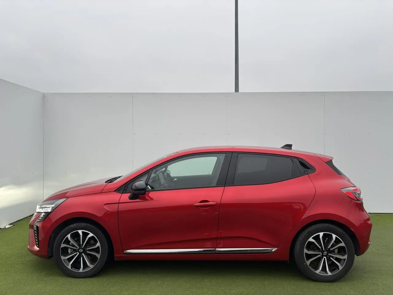 Profil droit d'une Renault Clio V 1.6 E-TECH Full Hybrid 2025 en rouge flamme métal avec jantes alliage 16 pouces.