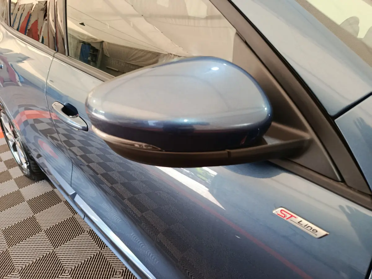 Rétroviseur côté gauche et badge ST Line sur la porte d’un Ford Kuga bleu vu en léger plongée.