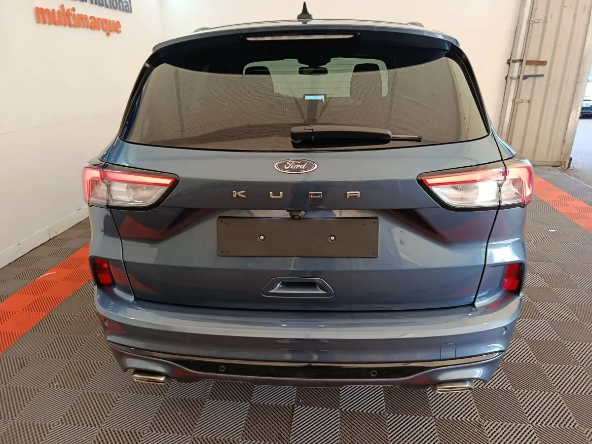 Vue arrière d'un Ford Kuga bleu 2024 avec feux LED et double sortie d'échappement dans un garage.