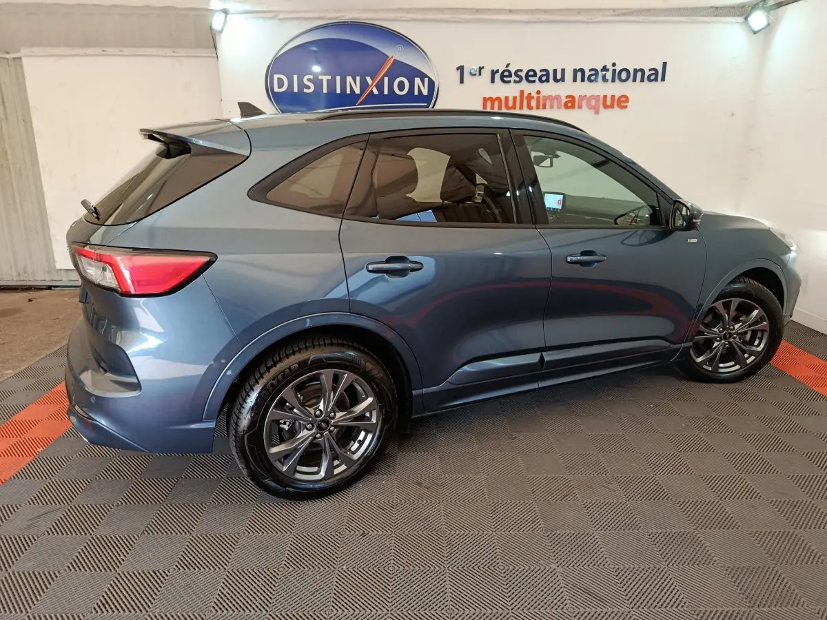 Ford Kuga 2024 bleu en vue profil côté droit, avec jantes alliage et vitres teintées dans un showroom.