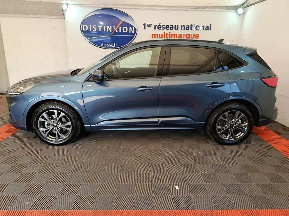Vue latérale droite d'un Ford Kuga 2024 bleu métallisé avec jantes alliage et vitres teintées dans un showroom.