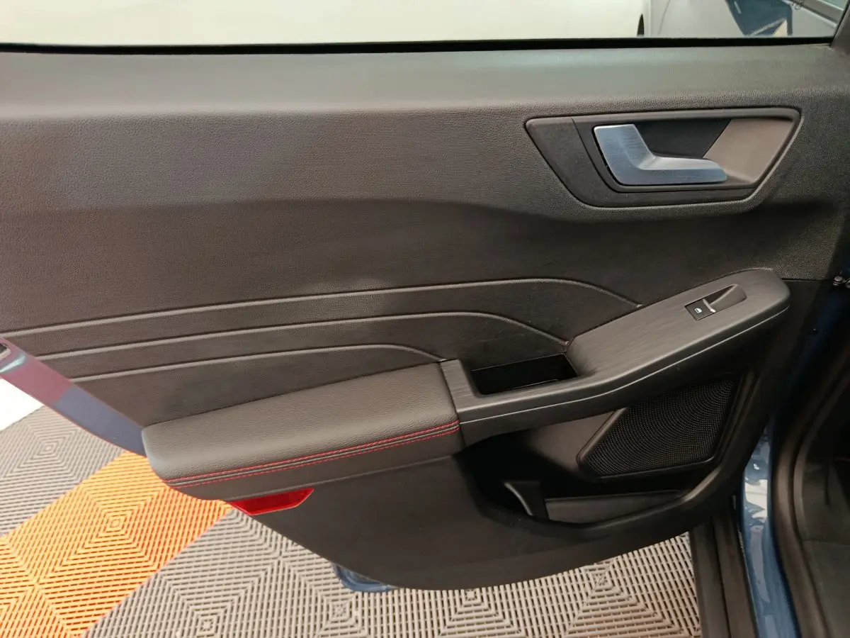 Gros plan sur la porte avant gauche intérieure noire avec surpiqûres rouges du Ford Kuga bleu 2024 St Line