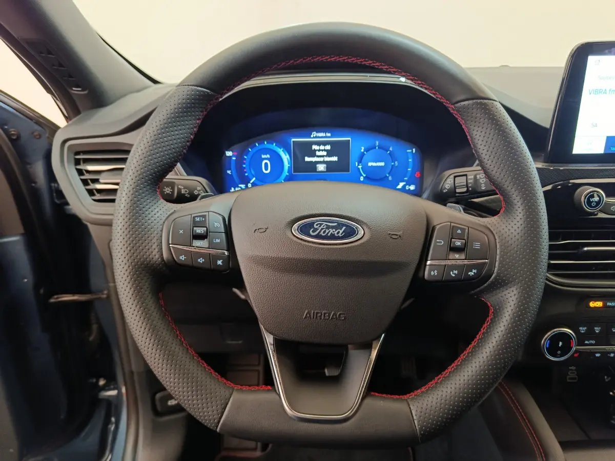 Vue rapprochée du volant en cuir noir avec surpiqûres rouges du Ford Kuga bleu 2024, tableau de bord digital visible.