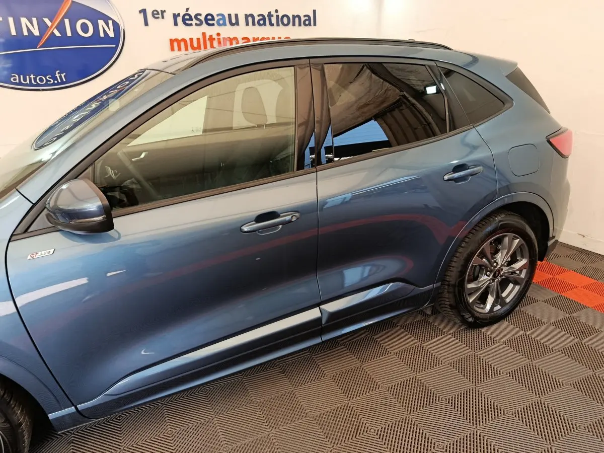 Vue latérale côté gauche d'un Ford Kuga bleu 2024 finition ST Line avec jantes alliage et rétroviseur électrique.