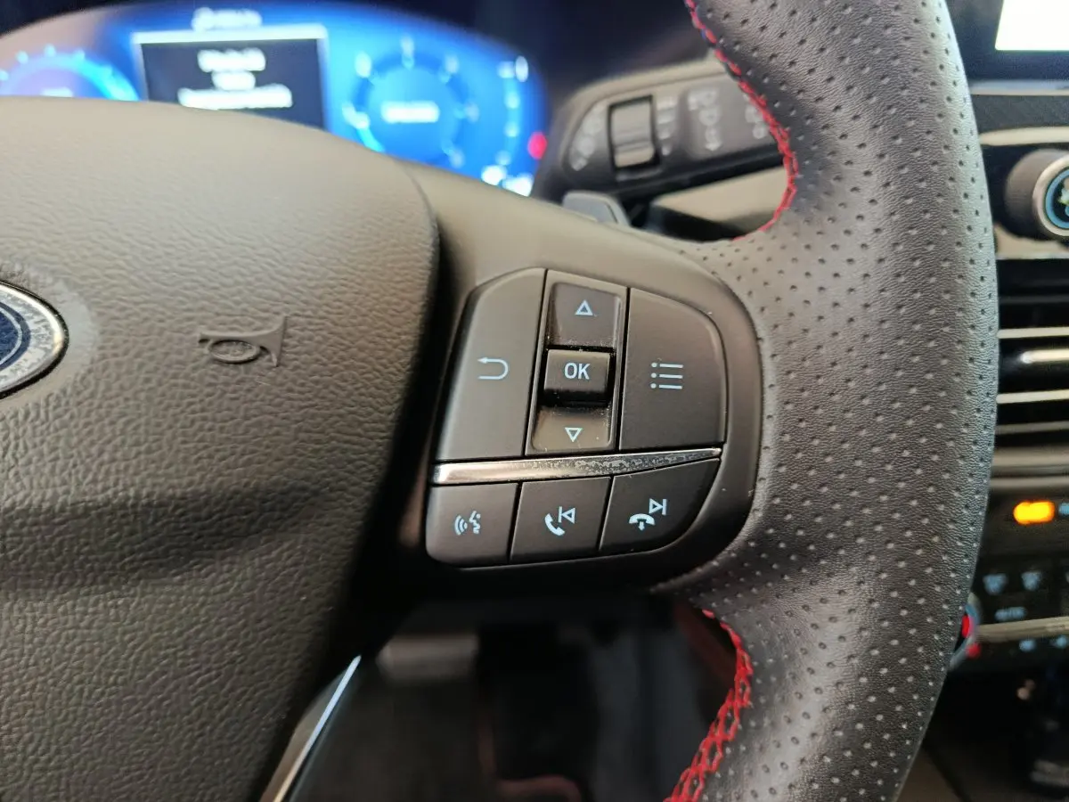 Gros plan sur les commandes du volant côté droit en cuir perforé avec surpiqûres rouges du Ford Kuga 2024 St Line.