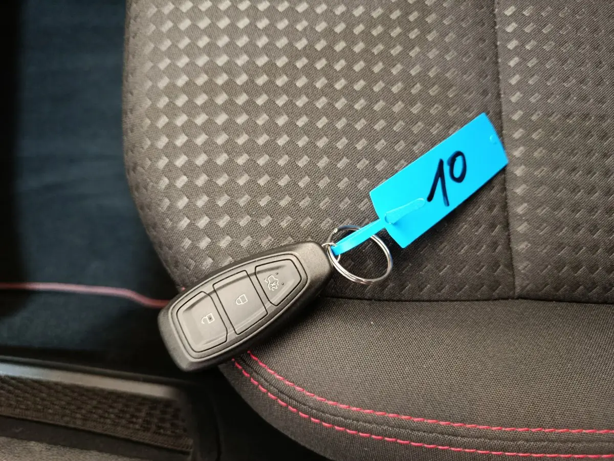 Télécommande de clé Ford posée sur siège tissu noir avec surpiqûres rouges dans un Ford Kuga 2024 St Line.